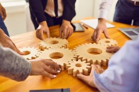 a group of business people holding wooden gears together